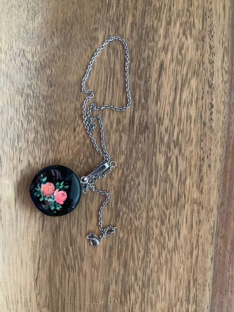 The photo shows a wooden pendant on a silver chain lying on a wooden surface. The pendant is made of black wood. On it are 2 large pink rosebuds painted in green leaves. Everything is varnished and therefore the reflection of my photographing hands can be seen on the pendant. I found this pendant in an old drawer in an abandoned house. It brought back memories of my grandmother showing me pendants, embroidery thread boxes and postcards in her little room. Everything was organized with love and care. My grandmother passed away in September. I didn't get to hear her stories and hug her for the last time.